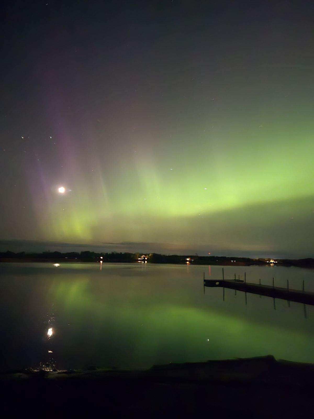 Northern lights sharing the sky with the moon above the dock.