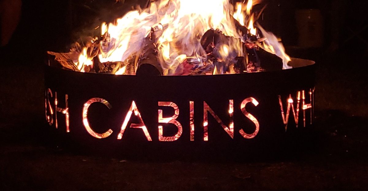 Our custom fire ring glowing at night, with Whitefish Cabins cut into the steel.