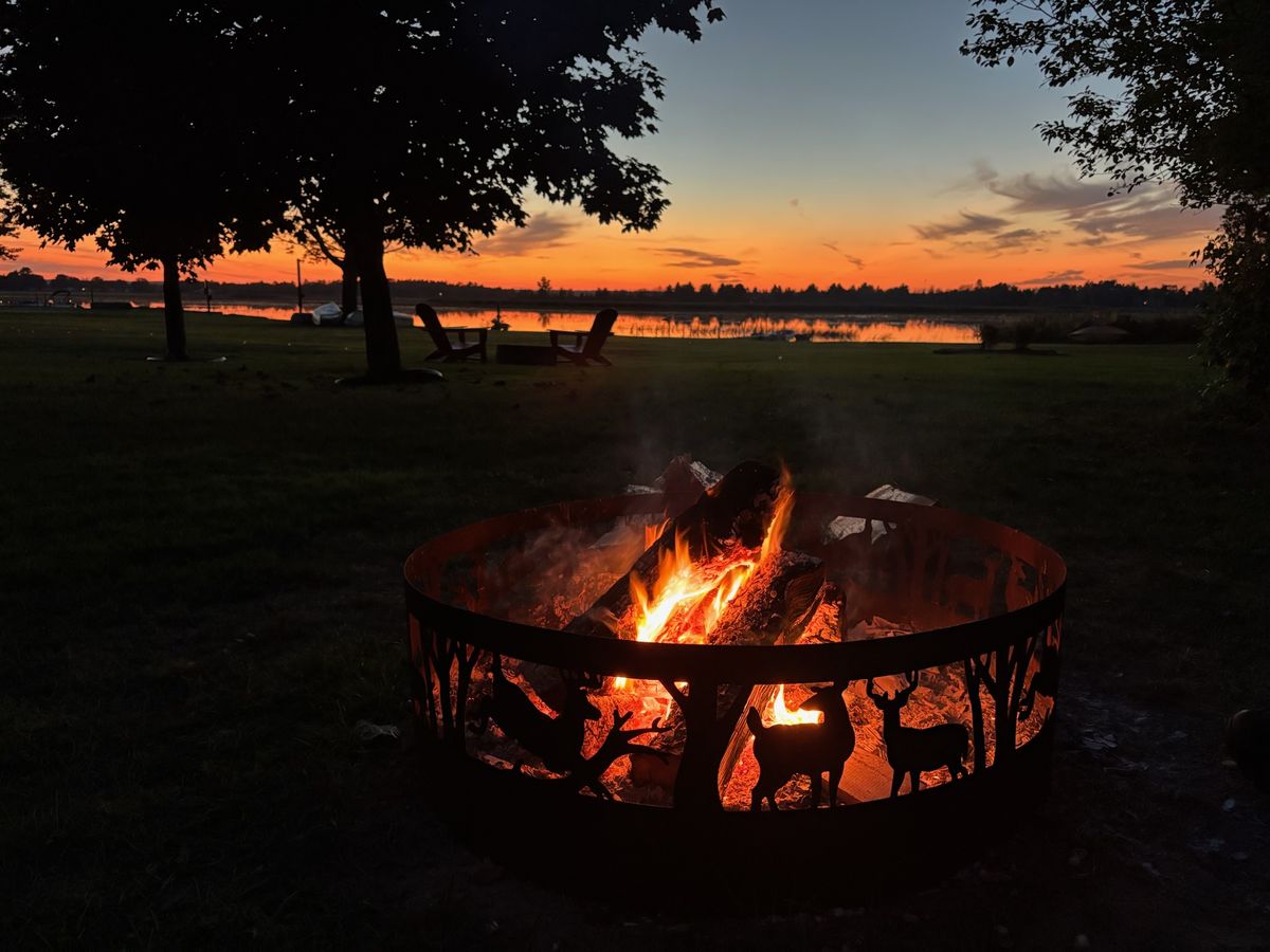 A fire blazing in the deer-silhouette fire ring at dusk, right by the water.