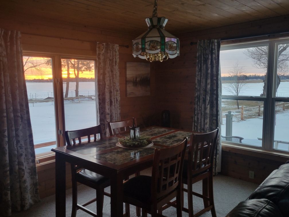 The lodge dining table set in front of windows glowing with a sunset over the bay.