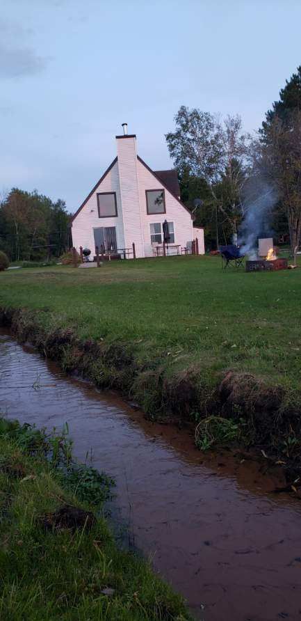 The white A-frame lodge beside the creek, with smoke curling from the chimney.