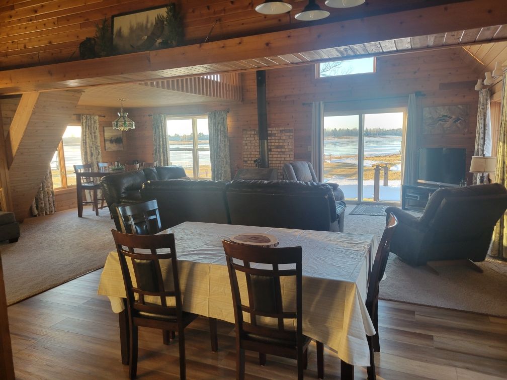 The open great room inside Whitefish Lodge, with the dining table and living area under big bay-view windows.