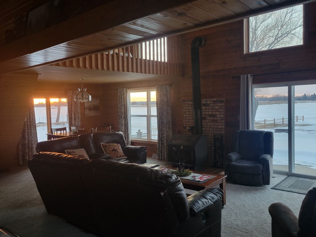 The lodge living room with the stove fireplace going and the lake through the windows.