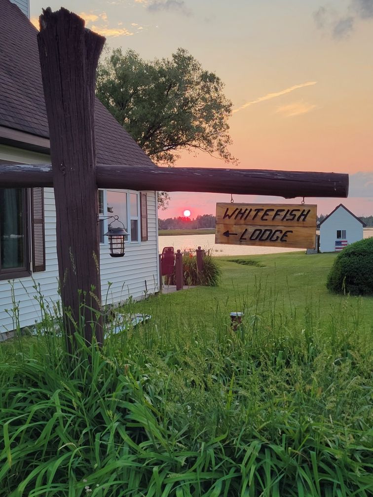 The wooden Whitefish Lodge sign with a sunset glowing behind it.