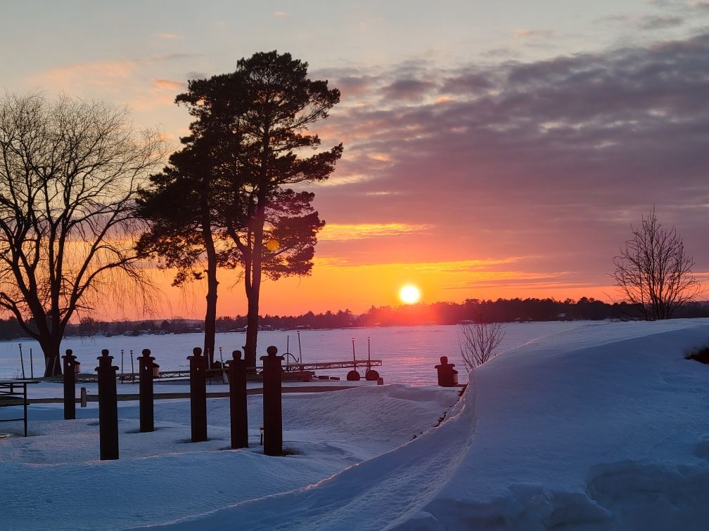 A winter sunset over the frozen bay, with the dock posts standing in the snow.